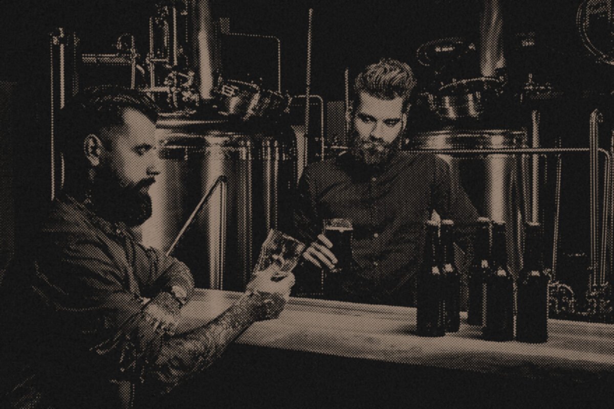 Two craft brewers tasting beside fermentation tanks